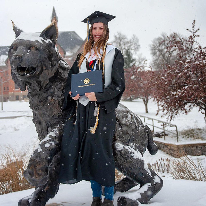 Graduate standing in the snow with statue of a bobcat.