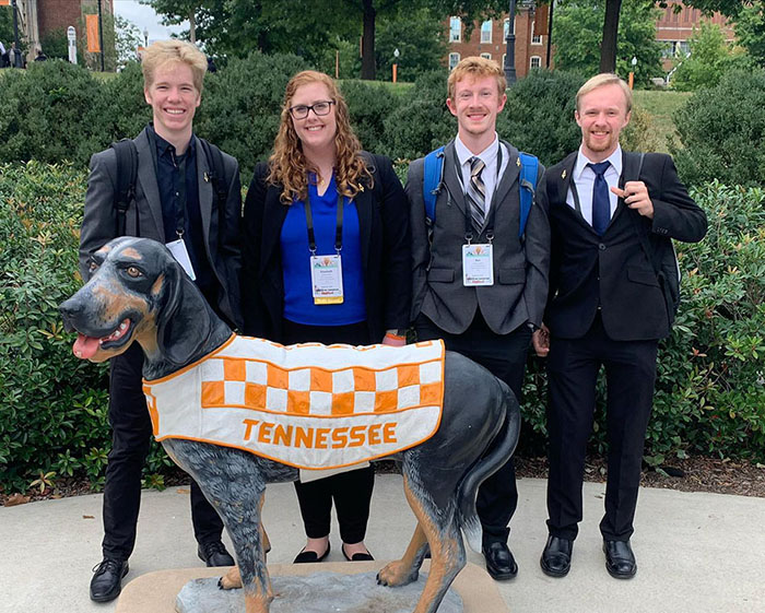 Group of students posing with statue of dog.