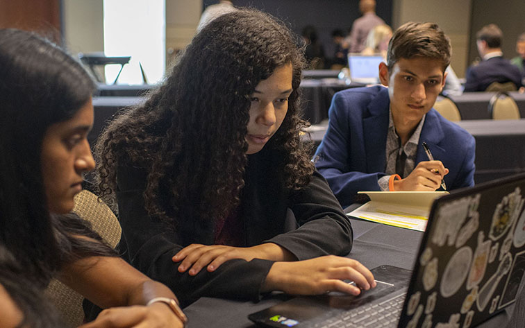 One student taking notes while another student uses her laptop.