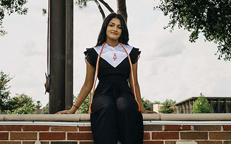 Female graduate sitting on a brick wall.