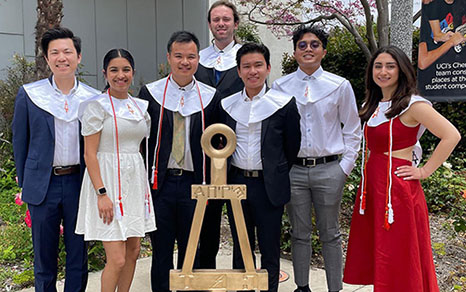 Tau Beta Pi chapter all wearing caps and gowns and posing around a Bent statue.