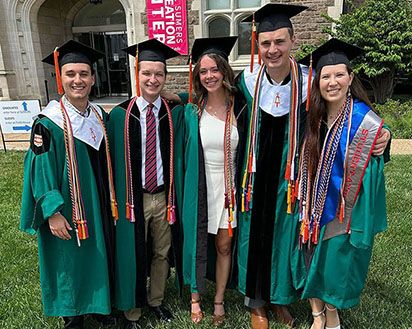 Five students in cap and gown after a graduation.