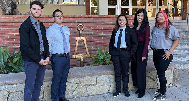 Five collegiate student members posing with statue of a Bent.