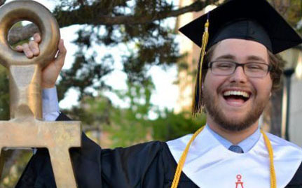 Tau Beta Pi member in cap and gown posing with statue of the Bent.