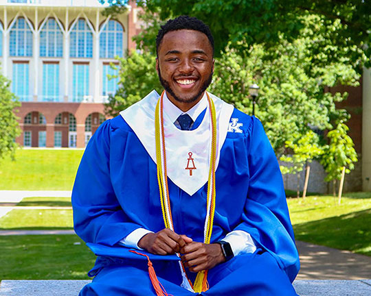 Male graduate sitting on a bench holding his cap.